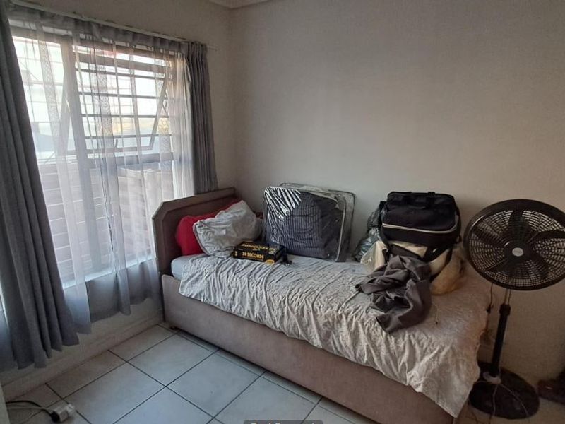 A standard bedroom featuring tiled flooring and a window fitted with security bars, offering a functional space for rest.