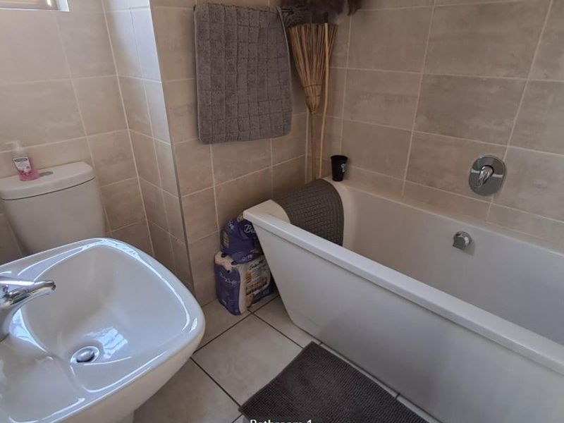 A functional bathroom featuring neutral ceramic wall and floor tiles, a modern pedestal basin, and a clean white freestanding bathtub.