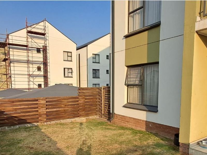 Rear view of the apartment featuring a small private garden area, timber fencing, and a tiled patio space.