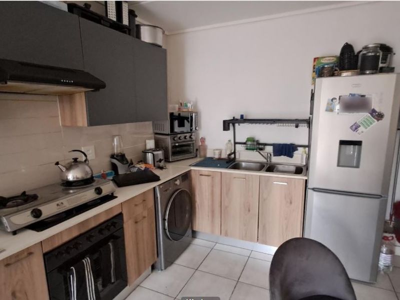 A functional kitchen featuring wood-look cabinetry, a gas hob with extractor fan, built-in oven, and tiled flooring with a double sink.