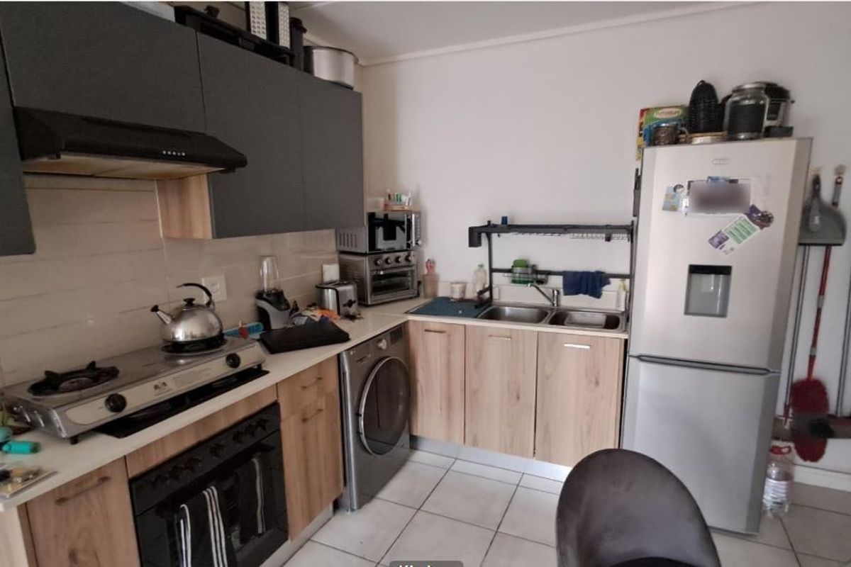 A functional kitchen featuring wood-look cabinetry, a gas hob with extractor fan, built-in oven, and tiled flooring with a double sink.