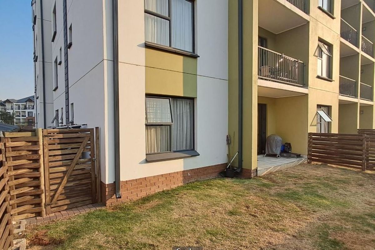 Rear view of the apartment building featuring a private garden area, wooden fencing, and access to a balcony with metal railings.