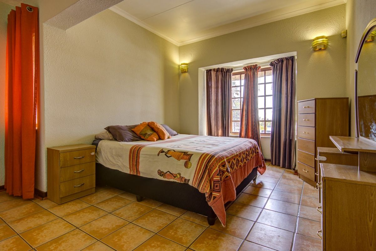 A bedroom featuring tiled flooring, wall-mounted light fixtures, and a window with natural light.