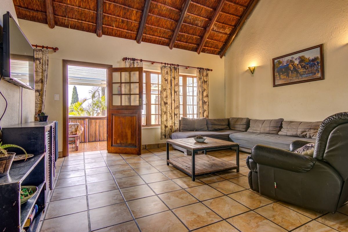 Spacious living room featuring a high vaulted thatched ceiling, ceramic floor tiles, and direct access to an outdoor patio area.