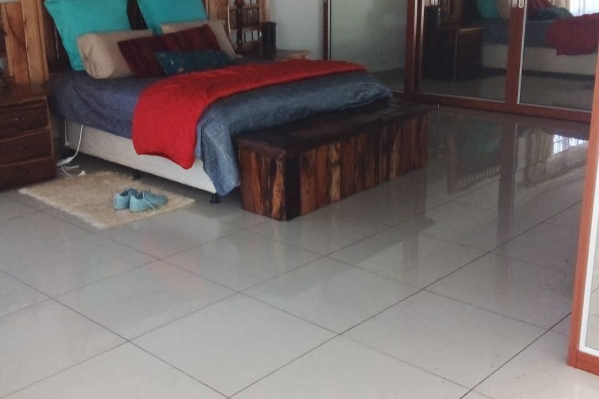 Spacious bedroom featuring large built-in mirrored wardrobes and neutral tiled flooring, requiring minor finishing touches to the ceiling area.