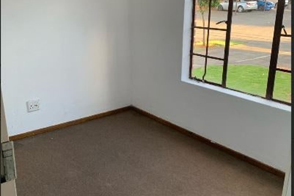 An empty bedroom featuring carpeted flooring, a steel-framed window, and a wall-mounted light fixture, ready for renovation or staging.
