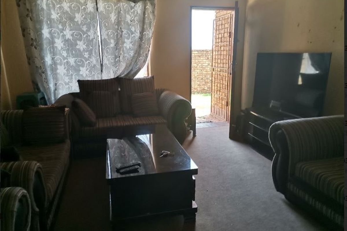 A living room area featuring carpeted flooring and direct access to an exterior space through a security gate.