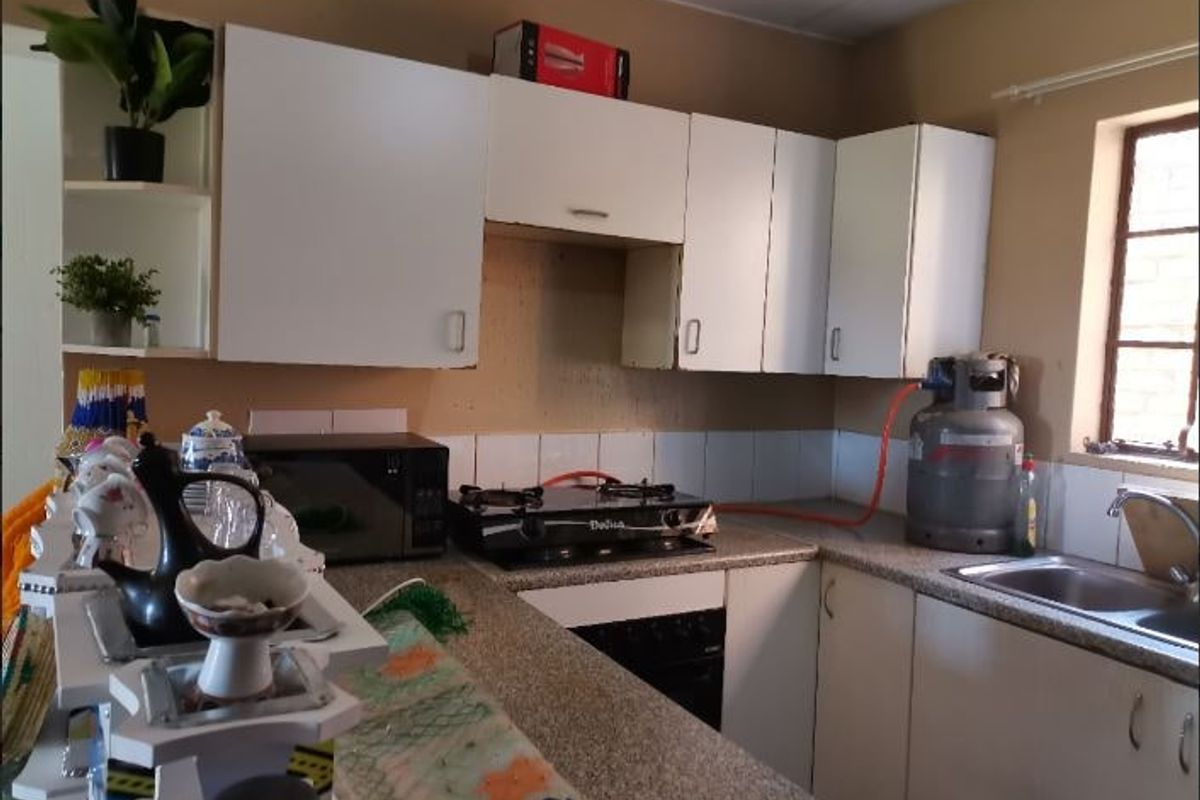 A functional kitchen featuring laminate countertops, white cabinetry, a gas hob, and a stainless steel sink with tiled splashback.