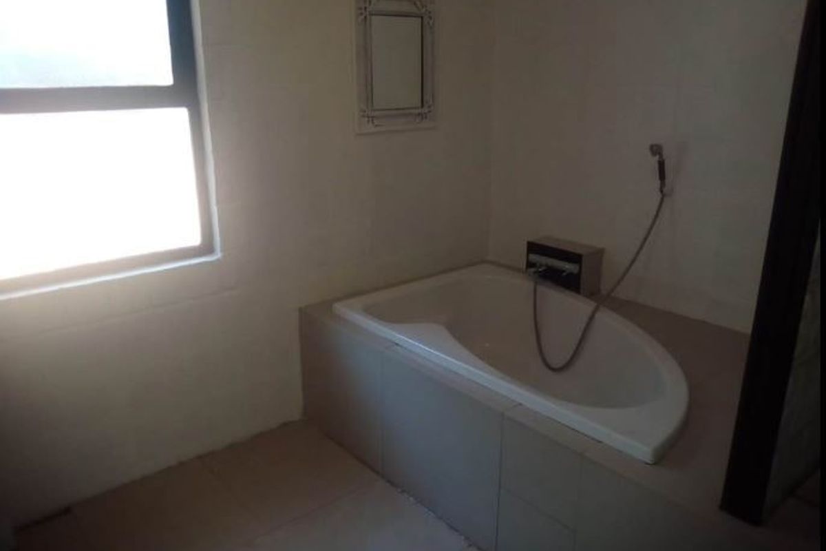 A functional bathroom featuring a built-in bathtub with a handheld shower mixer and tiled surround, offering a blank canvas for renovation.