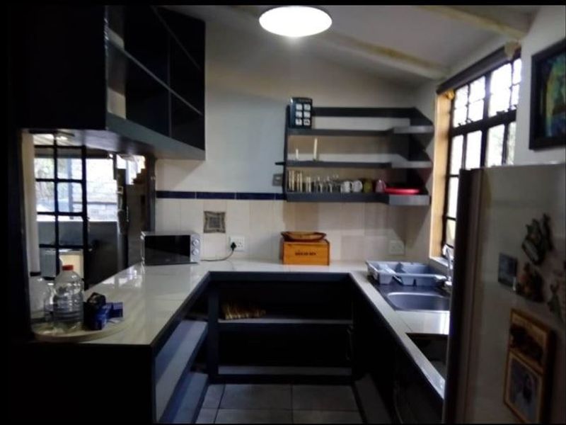 A functional kitchen featuring u-shaped cabinetry, open shelving, a tiled backsplash, and a stainless steel sink with natural light from a window.