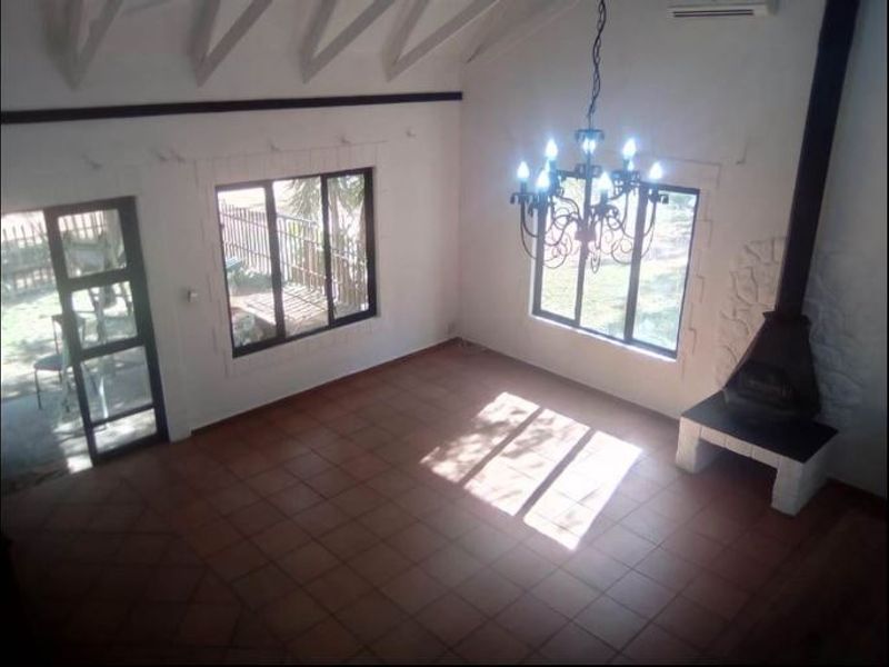 Spacious living area featuring vaulted ceilings with exposed rafters, tiled flooring, and a prominent freestanding fireplace with a stone surround.
