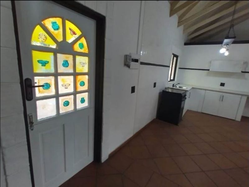 A functional kitchen area featuring tiled flooring, built-in cabinetry, a sink, and a distinctive stained glass entrance door under an exposed beam ceiling.