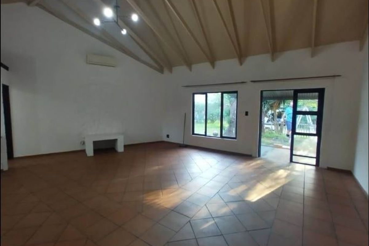 Spacious living area featuring high vaulted ceilings with exposed rafters, terracotta tile flooring, and direct access to the outdoor area through sliding glass doors.