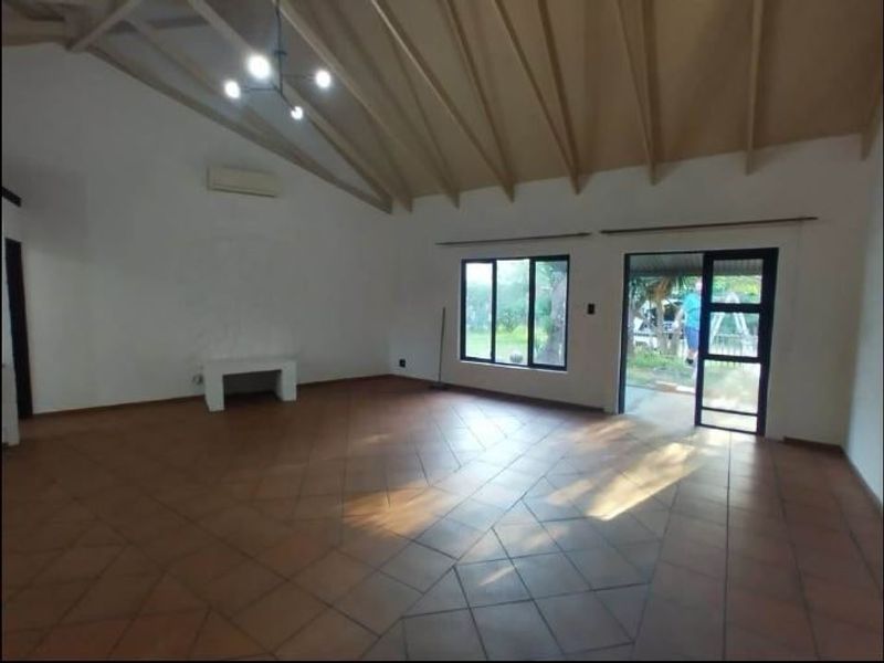Spacious living area featuring high vaulted ceilings with exposed rafters, terracotta tile flooring, and direct access to the outdoor area through sliding glass doors.