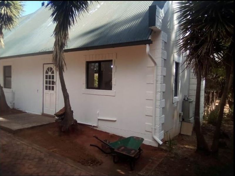 Rear view of a house featuring a corrugated metal roof, white painted walls with decorative quoins, and a paved walkway.