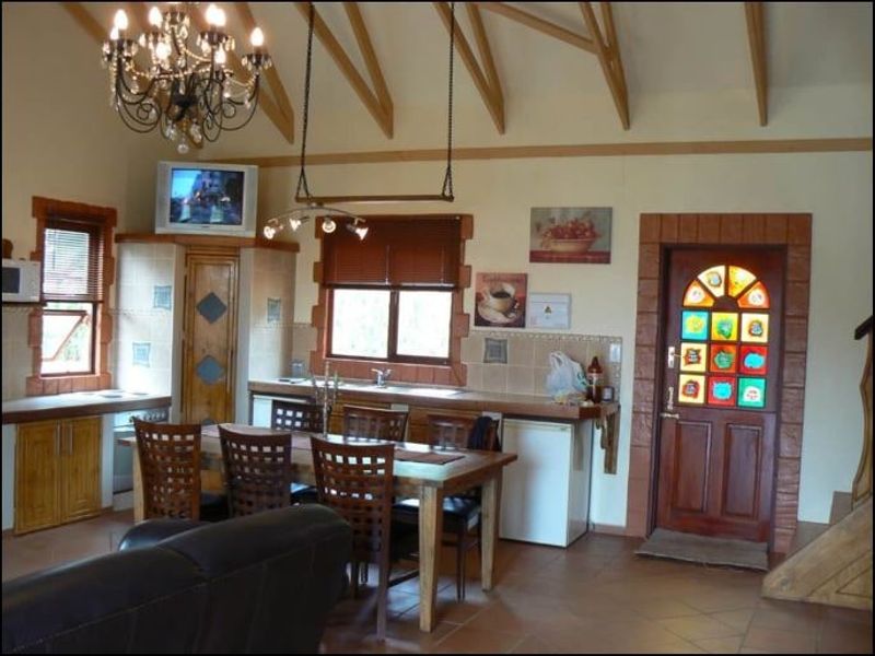 Open-plan living and kitchen area featuring vaulted ceilings with exposed timber rafters, tiled flooring, and a distinctive stained glass entrance door.