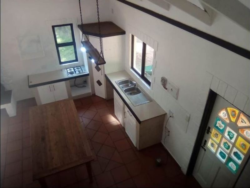 A functional kitchen featuring tiled flooring, built-in cabinetry, a gas hob, and a double bowl sink, complemented by exposed timber ceiling beams.