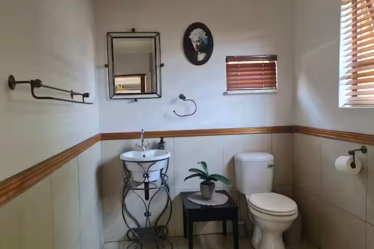 A compact bathroom featuring a pedestal basin, toilet, tiled wainscoting with timber trim, and venetian blinds.