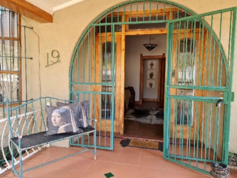 Front entrance featuring a distinctive arched green security gate, wooden door frame, and tiled porch area.