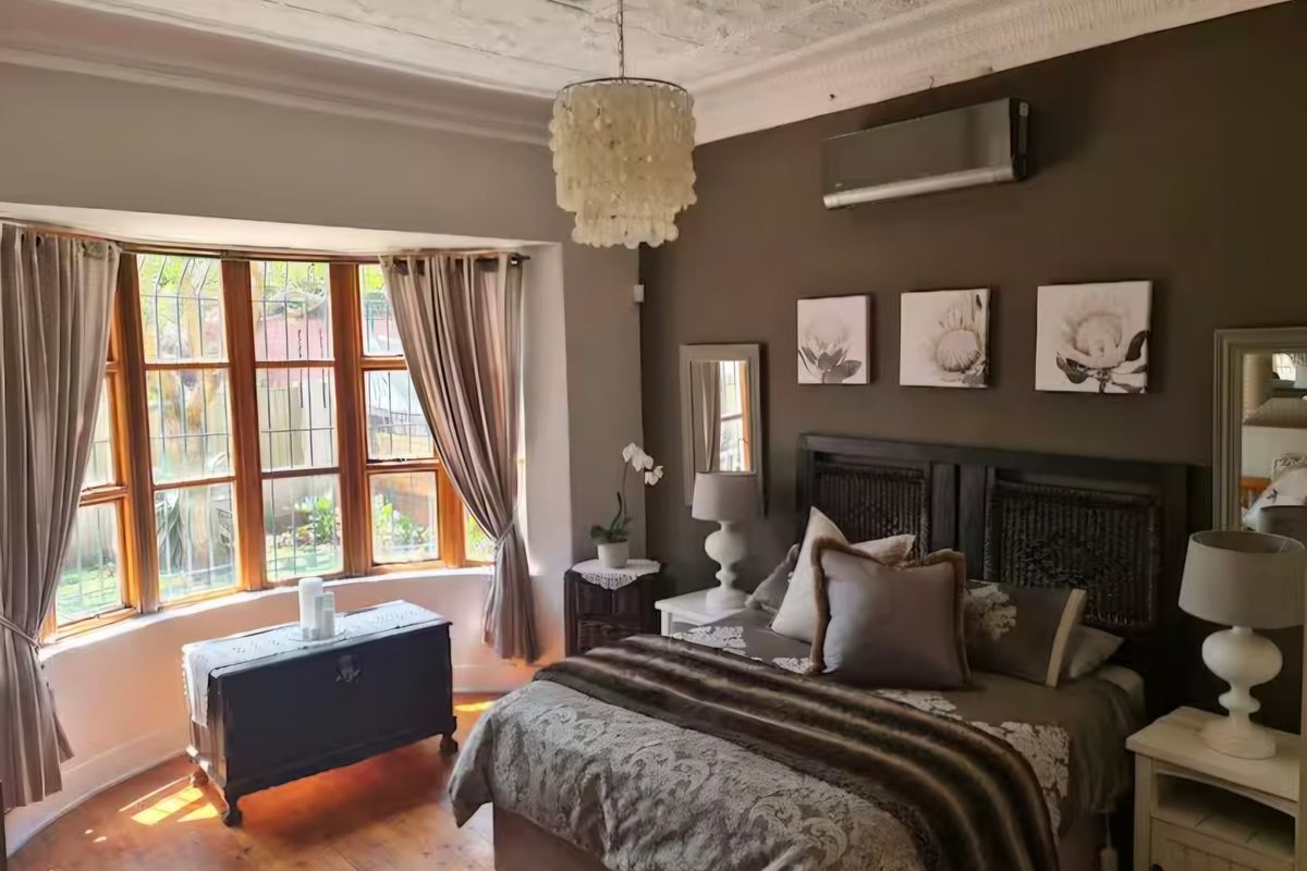 A well-maintained bedroom featuring timber flooring, a bay window, and a split-system air conditioner, complemented by an ornate pressed metal ceiling.