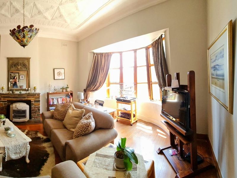 A character-filled living room featuring an ornate plaster ceiling, timber flooring, and a prominent stone fireplace with a large bay window.