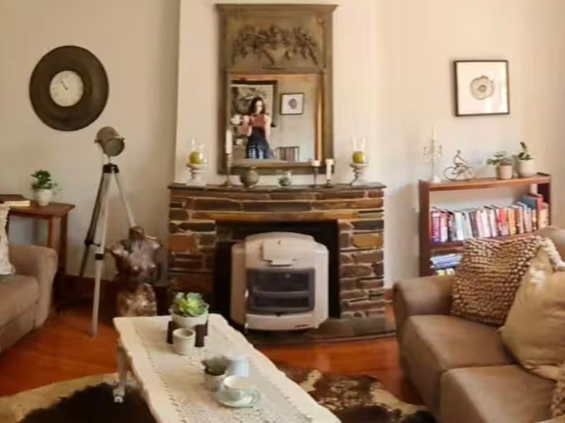 A cozy living room featuring a traditional stone fireplace with a gas heater insert, ornate ceiling detailing, and polished hardwood flooring.