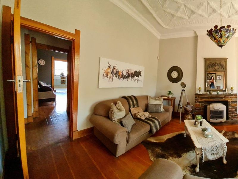 A character-filled living room featuring an ornate plaster ceiling, hardwood floors, and a brick fireplace, with a view into the adjacent room.