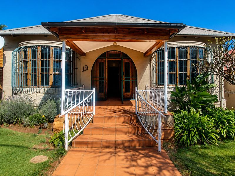 Front elevation of a character home featuring a tiled entrance porch, arched doorway, and metal security window grilles set within a landscaped garden.