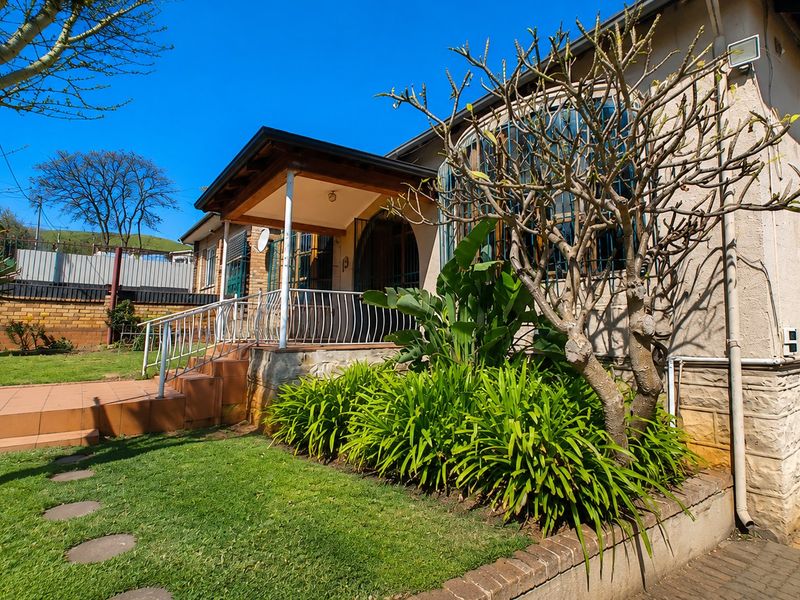 Front elevation of the house featuring a covered porch, tiled entrance steps, security railings, and established garden landscaping.