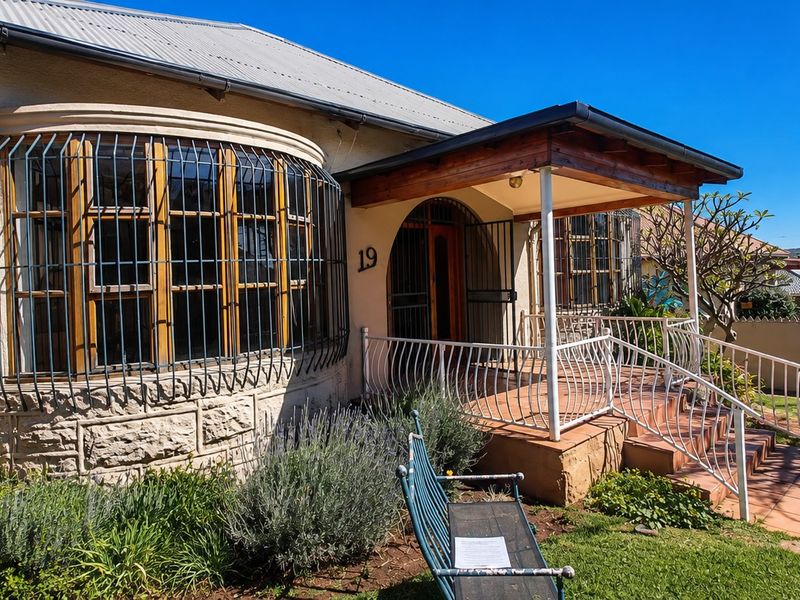 Front facade of a house featuring a covered porch, stone masonry detailing, security bars on windows, and a tiled entrance area.