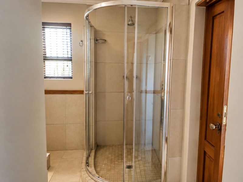 A functional bathroom featuring a curved glass shower enclosure, neutral wall and floor tiling, and a classic timber door.