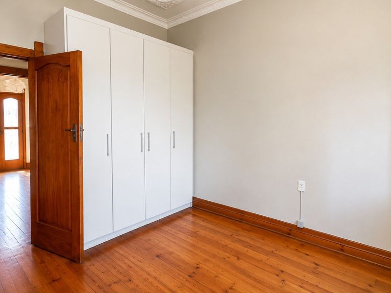 A bright, empty bedroom featuring polished hardwood floors, built-in white cabinetry, and classic timber door frames.