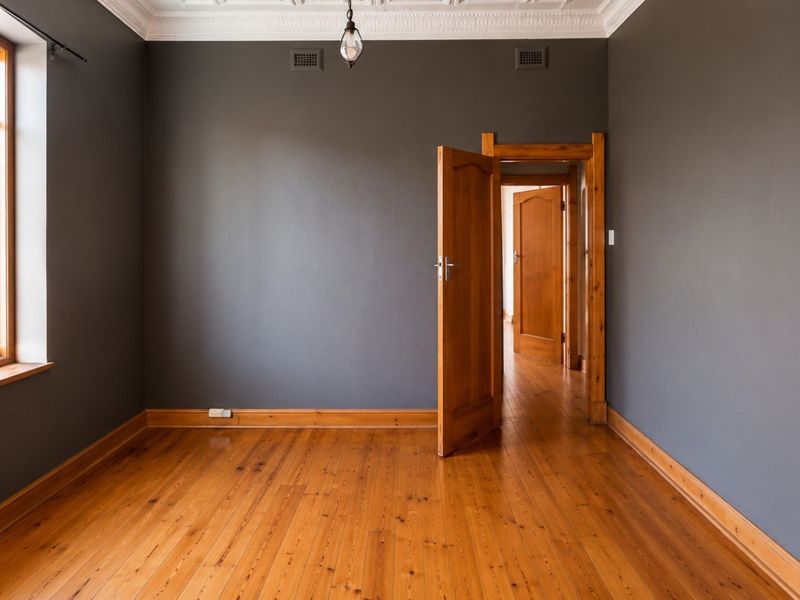 An empty bedroom featuring polished timber flooring, ornate ceiling cornices, and dark grey walls, providing a clean and neutral canvas.