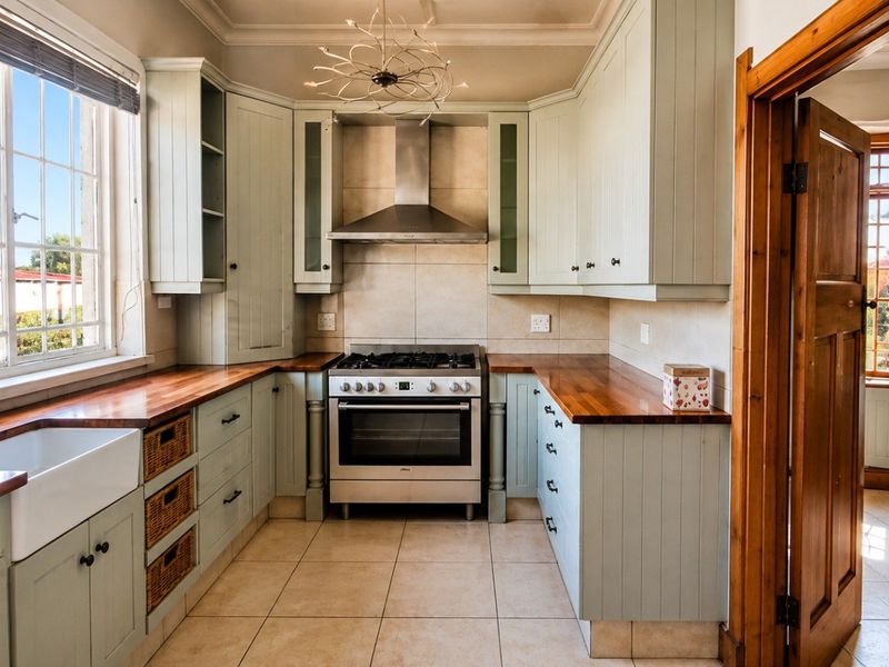 A well-maintained kitchen featuring light-toned cabinetry, wooden countertops, a farmhouse sink, and a stainless steel gas stove with an extractor fan.