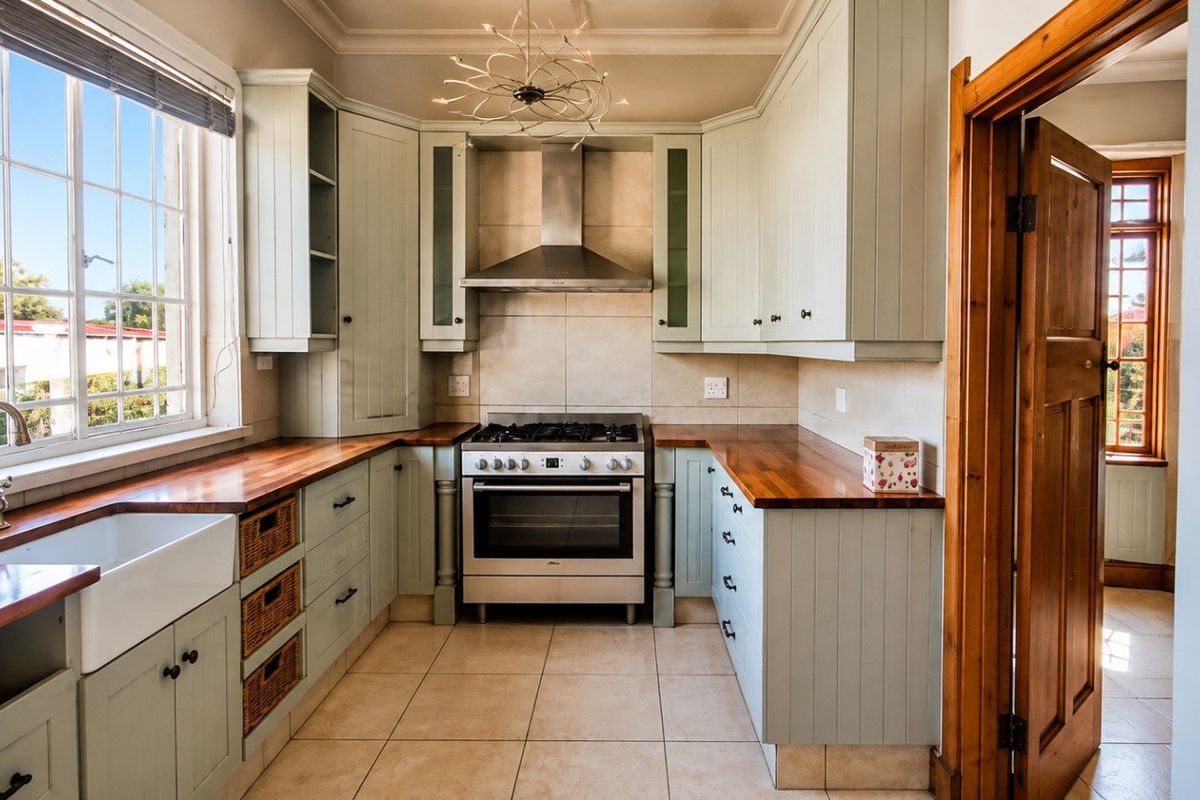 A well-maintained kitchen featuring light-toned cabinetry, wooden countertops, a farmhouse sink, and a stainless steel gas stove with an extractor fan.