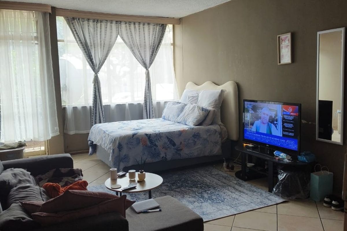 A bedroom featuring tiled flooring, textured ceilings, and large windows allowing natural light. The space is functional but would benefit from cosmetic updates.
