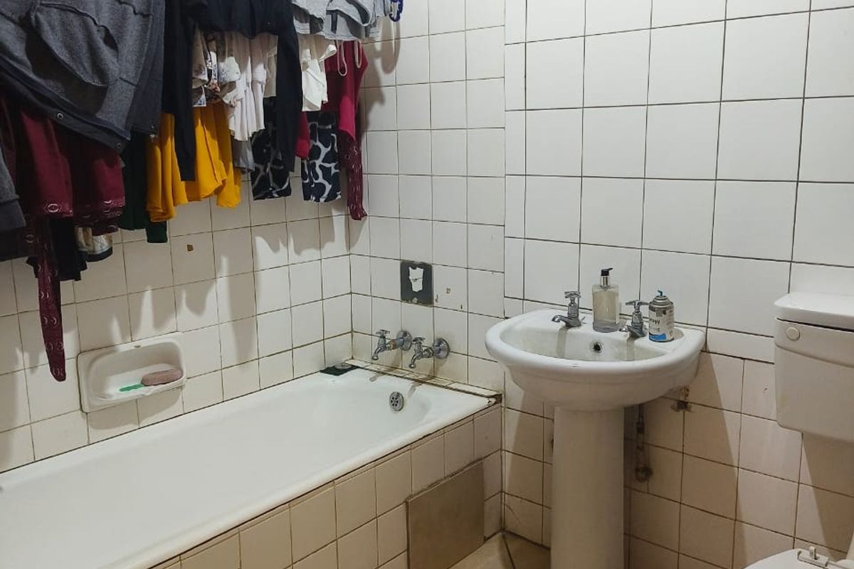 A dated bathroom featuring a pedestal basin, bathtub, and toilet with full-height wall tiling and louvered window ventilation.