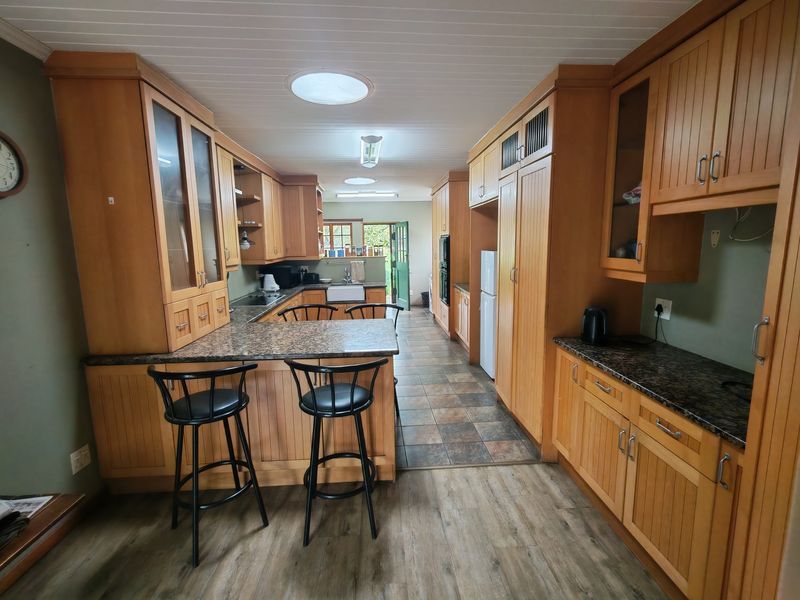 Spacious kitchen featuring extensive wooden cabinetry, granite countertops, a farmhouse sink, built-in oven, and a breakfast bar with direct access to the outdoors.