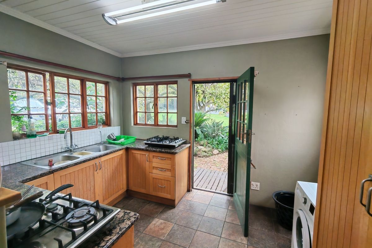 A functional kitchen featuring wooden cabinetry, granite countertops, gas hobs, and direct access to the garden through a timber door.