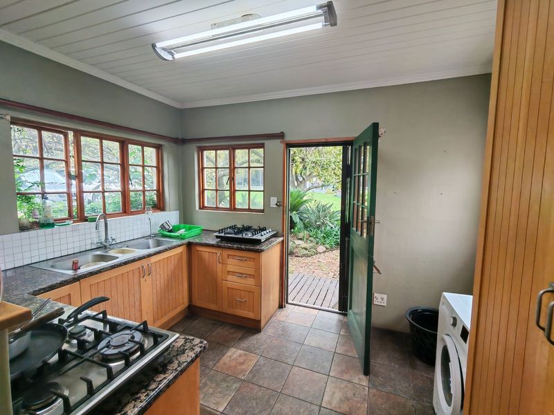 A functional kitchen featuring wooden cabinetry, granite countertops, gas hobs, and direct access to the garden through a timber door.