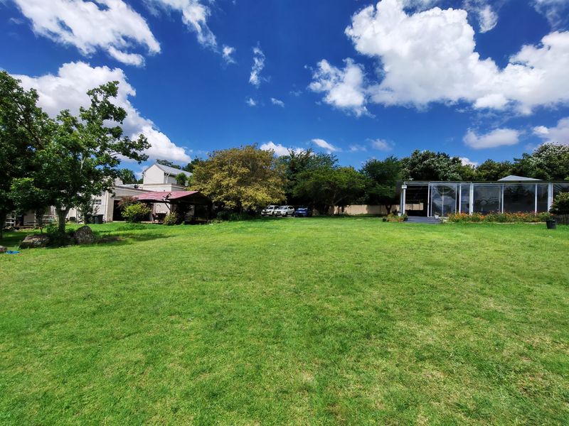 A spacious residential garden featuring a large lawn, mature trees, and a covered outdoor patio area.