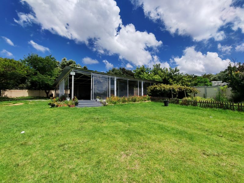 A spacious rear garden featuring a large enclosed patio structure with metal framing and roll-up vinyl curtains, set against a well-maintained lawn.