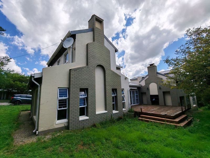 Rear view of the property featuring a brick chimney, timber deck, and built-in outdoor fireplace, set against a large garden area.