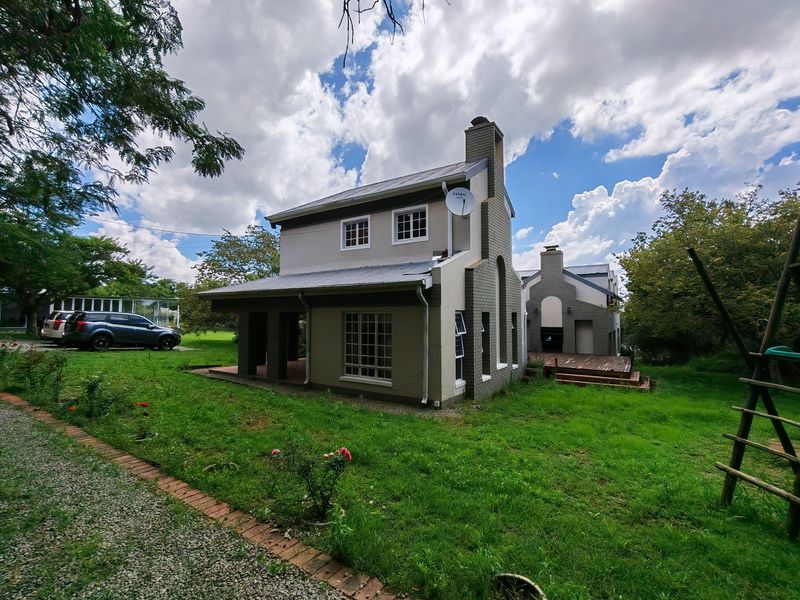 Rear view of a two-story residential property featuring a brick and rendered facade, metal roofing, a chimney, and an attached timber deck.