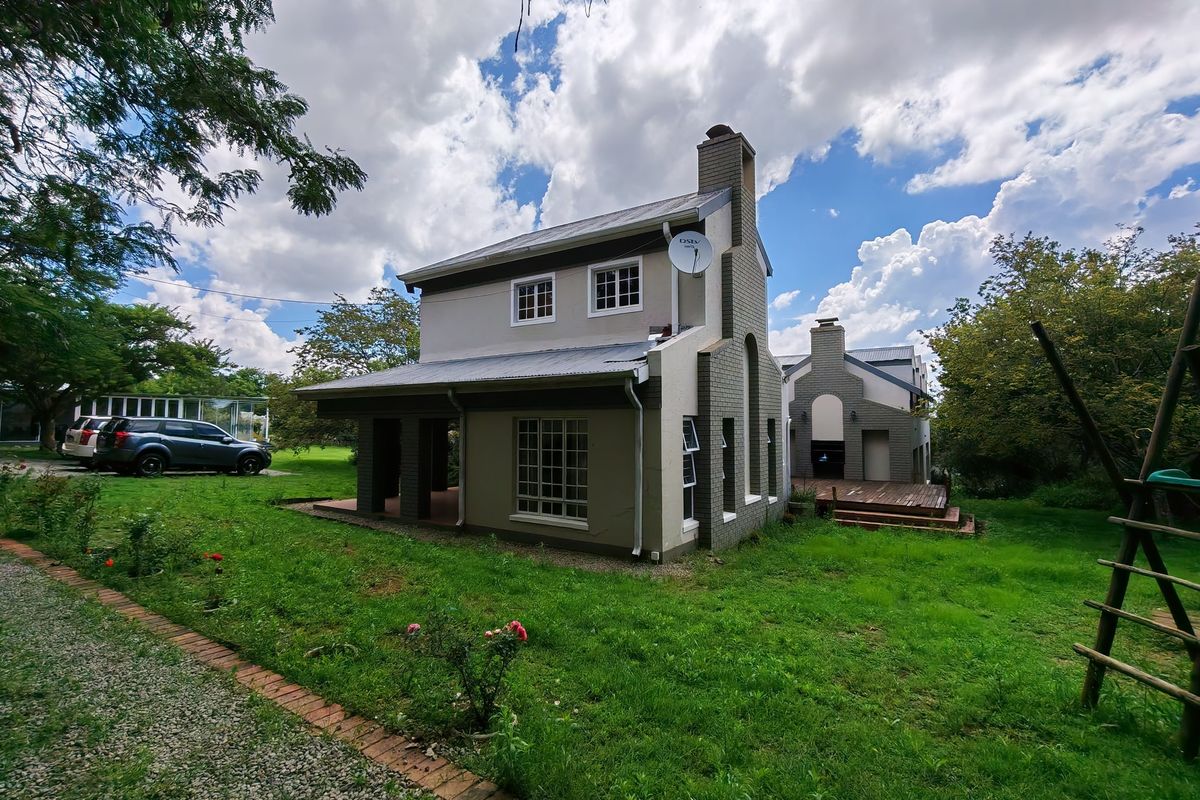 Rear view of a two-story residential property featuring a brick and rendered facade, metal roofing, a chimney, and an attached timber deck.