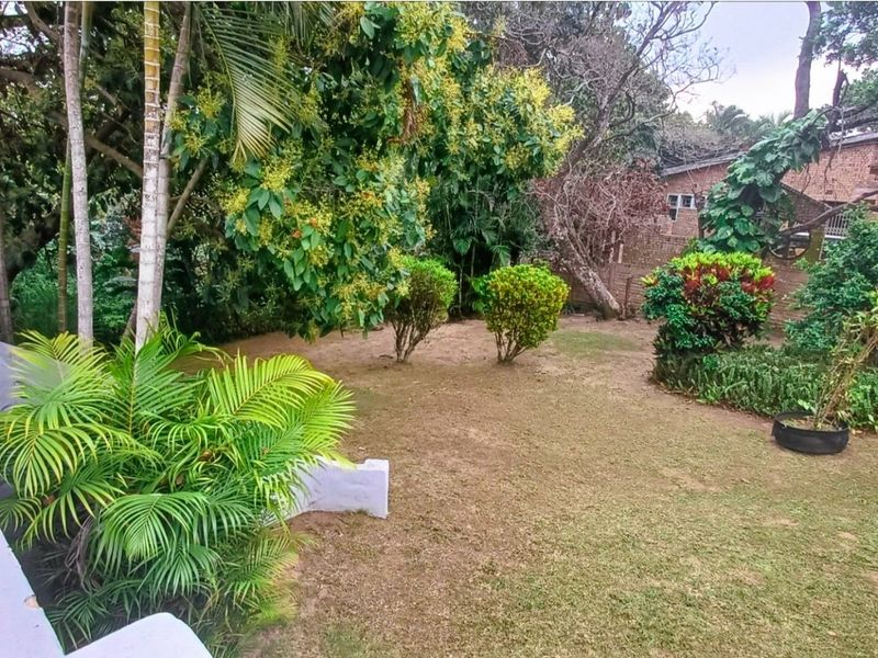 A private garden area featuring established trees, landscaped shrubs, and a brick boundary wall, offering a natural outdoor space.