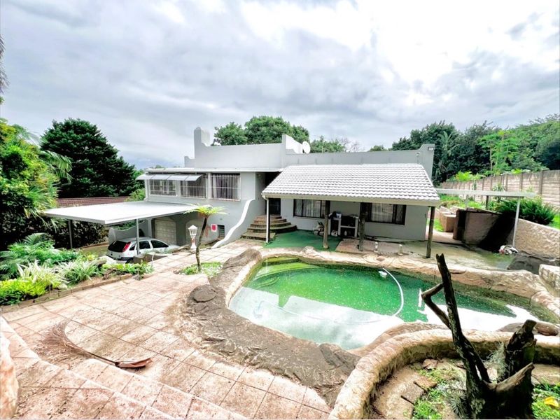 Rear exterior view featuring a swimming pool, paved patio area, and a covered carport attached to the main house structure.