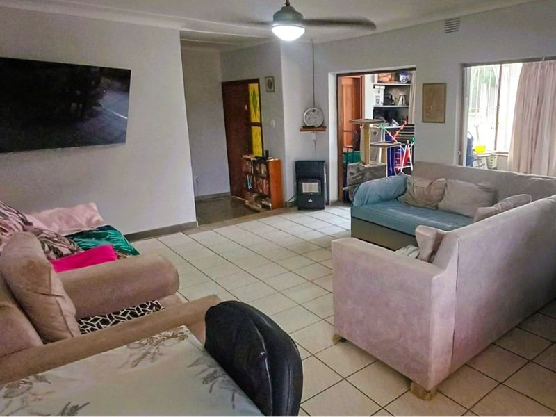A spacious living room featuring tiled flooring, a ceiling fan, and a gas heater, providing a functional and comfortable living area.