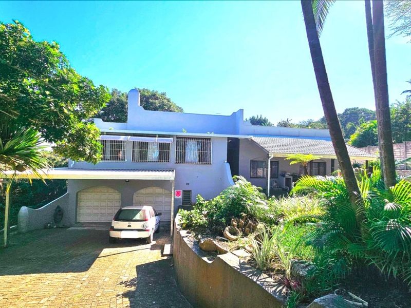 Front elevation of a multi-level house featuring a double garage, paved driveway, and established garden with a retaining wall.