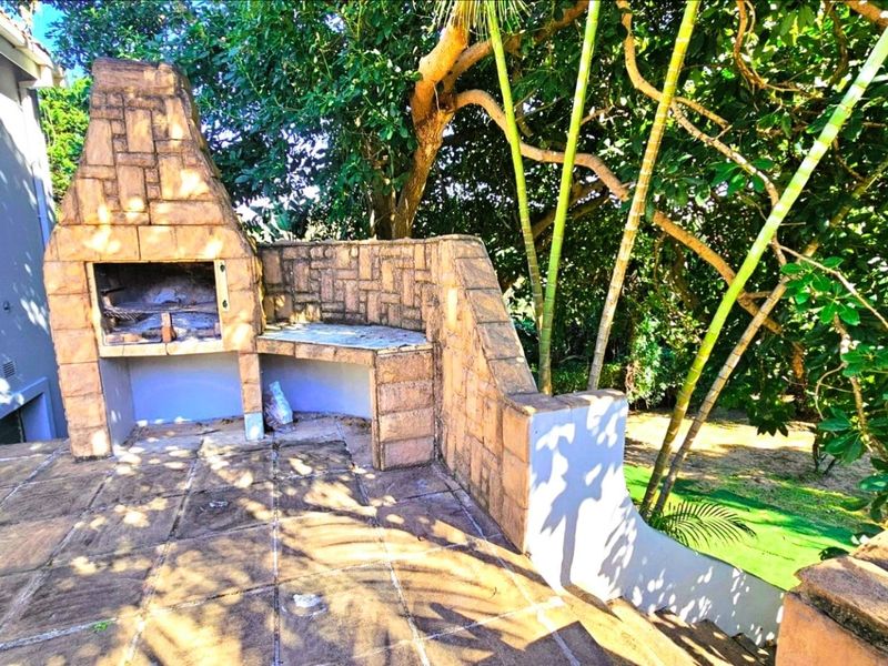 Outdoor patio area featuring a built-in stone braai and masonry counter, set in a garden environment.